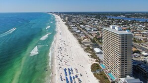 An aerial view of a coastal city with a beach, a high-rise hotel, and a marina.
