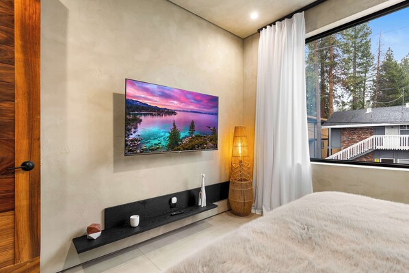 A bedroom with a large window, a painting of a landscape, a bedside table, and a fluffy rug. - Paradise South Lake Tahoe 2 Bedroom (Unit D) (South Lake Tahoe)