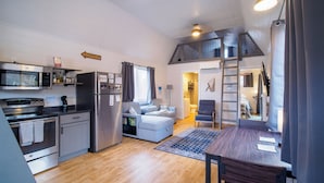 Una cucina compatta con elettrodomestici moderni, una zona pranzo con tavolo in legno e un angolo salotto accogliente con divano.