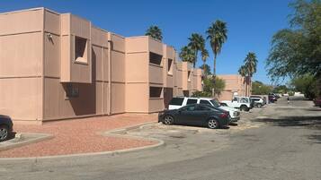 A row of beige buildings with a parking lot in front, palm trees, and a clear blue sky.