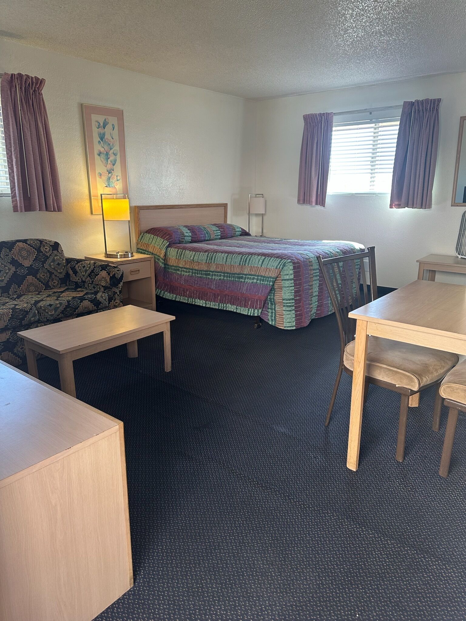 Una habitación de hotel con cama, sofá, escritorio, lámpara y ventana con cortinas.