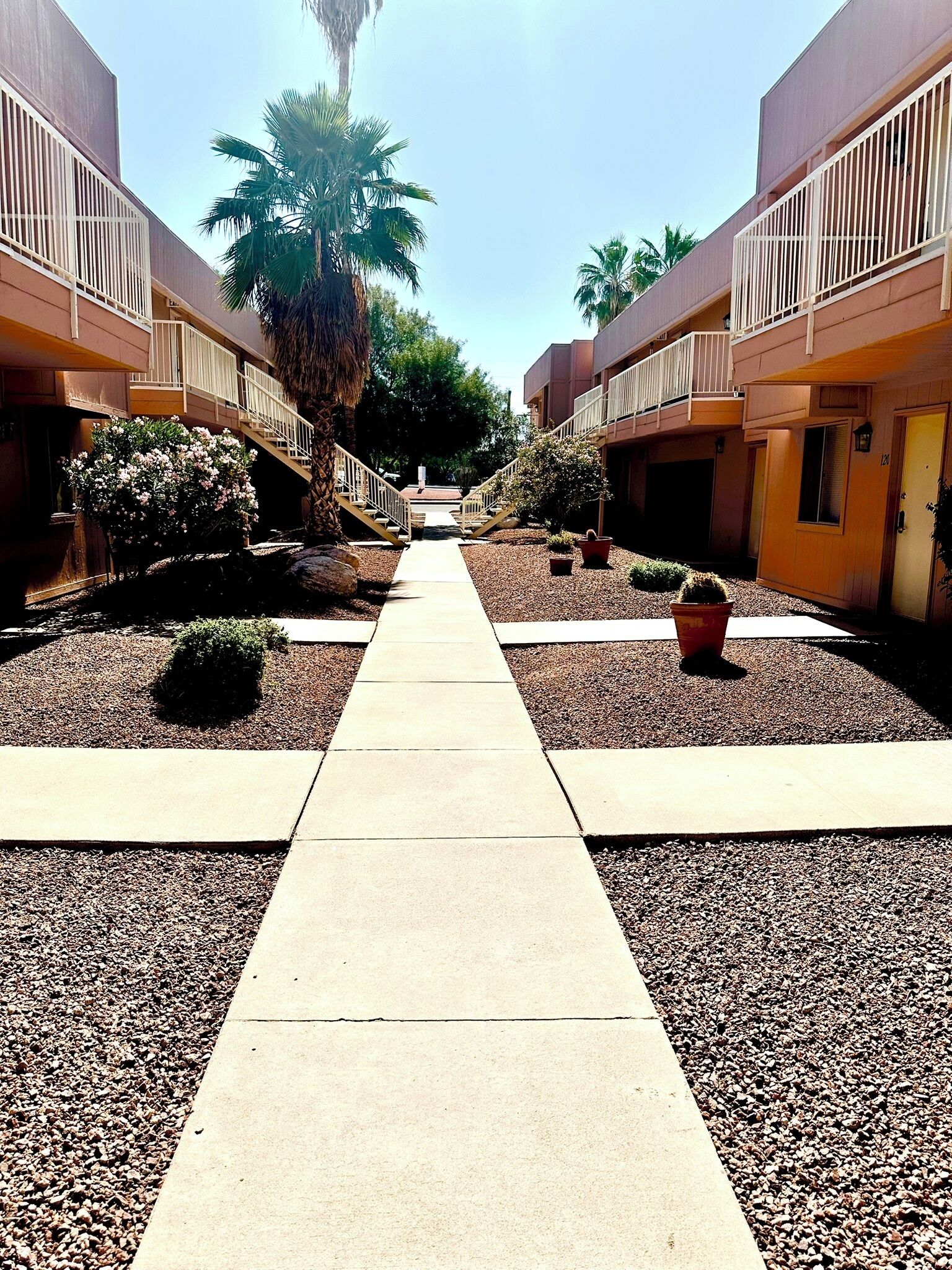 A pathway leading to a building with balconies, surrounded by gravel and potted plants.