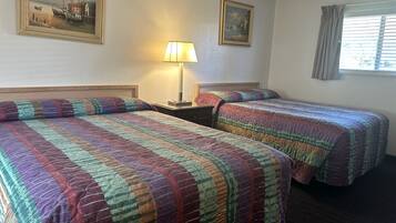 Une chambre d’hôtel avec deux lits, une table de chevet, une lampe et deux tableaux encadrés au mur.