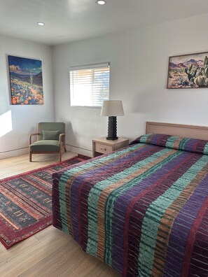 Un dormitorio con cama, una silla, una mesita de noche, una lámpara y dos cuadros en las paredes.