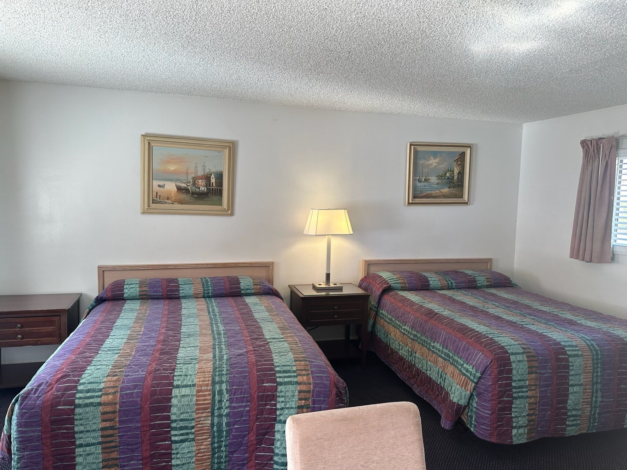 Une chambre d’hôtel avec deux lits, une table de chevet avec une lampe et deux tableaux encadrés au mur.