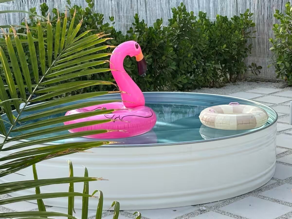 Ett runt bubbelbad med en rosa uppblåsbar flamingo och en beige uppblåsbar flotte, omgivet av grönska.