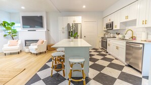 A modern kitchen with white cabinets, a central island, bar stools, a flat-screen TV, and a microwave. - Mediterranean-style Home Near Design District With a Pool! (Miami)