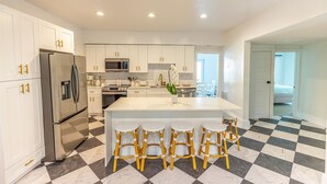 A modern kitchen with white cabinets, a stainless steel refrigerator, a central island with bar stools, and a checkered floor. - Mediterranean-style Home Near Design District With a Pool! (Miami)