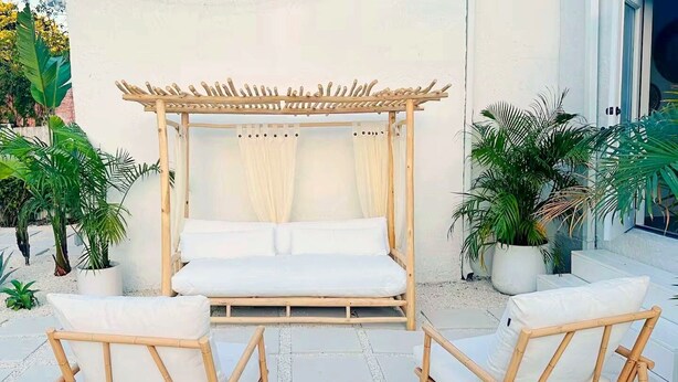 A wooden bed with white bedding, two wicker chairs, and potted plants around a patio area. - Mediterranean-style Home Near Design District With a Pool! (Miami)