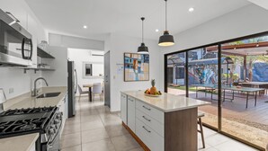 Une cuisine moderne dotée d’un îlot central, d’appareils électroménagers en acier inoxydable et d’un coin repas offrant une vue sur la terrasse extérieure.