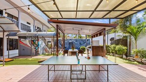 Un espace extérieur abrité comprenant une table de ping-pong, des sièges et une vue sur une aire de jeux.