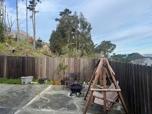 Un jardin avec une clôture en bois, un barbecue, une balançoire en bois et, au loin, une vue sur le paysage urbain.
