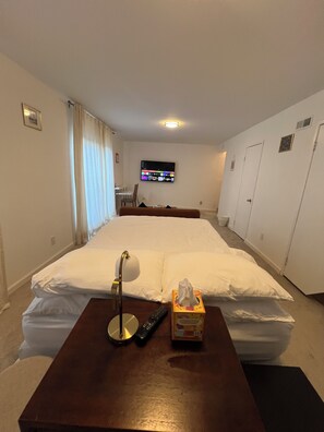 Une chambre d’hôtel avec un lit, une table de chevet avec une lampe et une télécommande, un téléviseur fixé au mur et une fenêtre avec des rideaux.