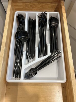 Un tiroir compartimenté contenant des couverts noirs, notamment des fourchettes, des couteaux et des cuillères.