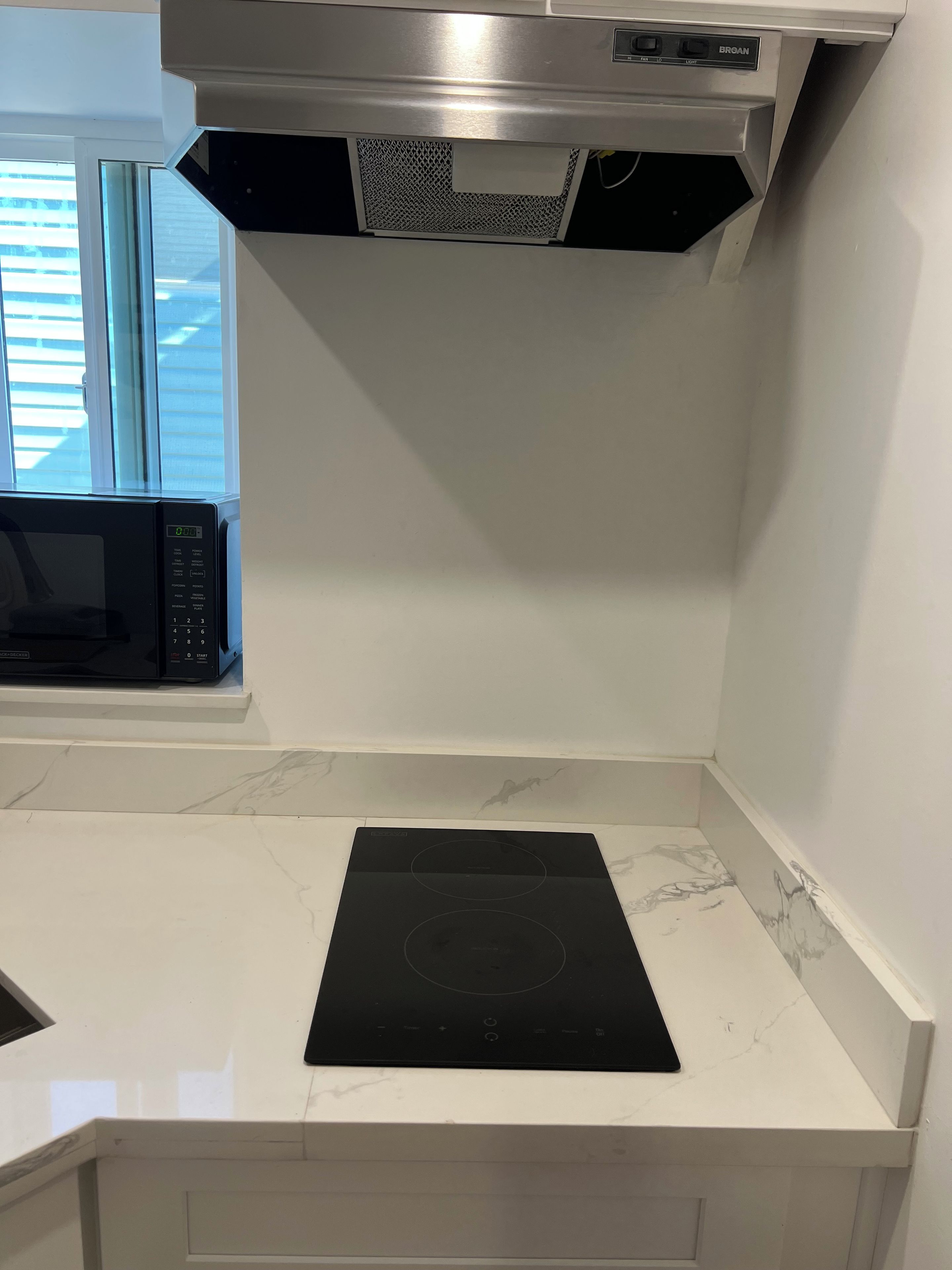 A kitchen with a microwave, an induction cooktop, and a stainless steel range hood.