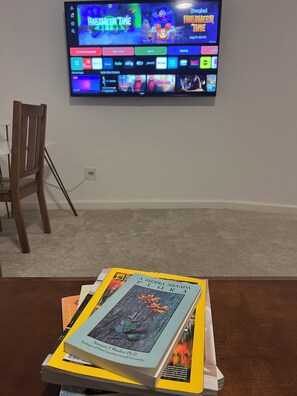 Un téléviseur à écran plat fixé au mur affiche différents services de diffusion en continu. Devant le téléviseur, on trouve une table sur laquelle est posée une pile de livres.