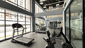 Une salle de sport équipée de tapis de course, de vélos d’exercice et d’appareils de musculation, dotée de grandes fenêtres et d  ’un design moderne au niveau du plafond.