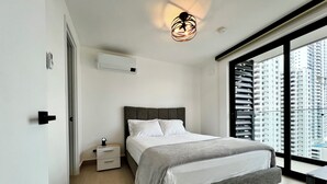 Une chambre moderne avec un lit, une table de chevet et une vue sur des immeubles de grande hauteur.