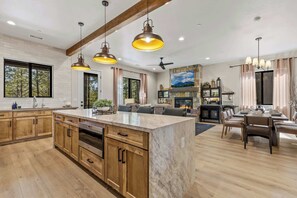 A spacious kitchen with wooden cabinets, a marble island, pendant lighting, and a dining area with a fireplace. - NEW! | Single-Level | Hot Tub | AC | Int Design (Flagstaff)