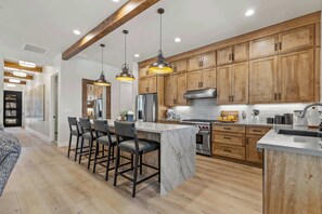 A modern kitchen with wooden cabinets, a marble island, bar stools, pendant lighting, and stainless steel appliances. - NEW! | Single-Level | Hot Tub | AC | Int Design (Flagstaff)