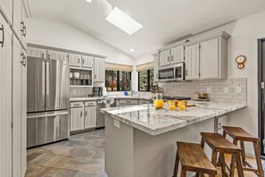 A modern kitchen with white cabinetry, a stainless steel refrigerator, a microwave, and a large island with bar stools. - NEW! | Kachina Cabin | AC | Trail Access | Hot Tub (Flagstaff)