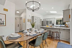 A modern kitchen with white cabinets, a dining area with a wooden table and chairs, and a chandelier. - NEW! | Kachina Cabin | AC | Trail Access | Hot Tub (Flagstaff)