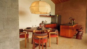Een eetgedeelte met een ronde tafel, stoelen, een hanglamp, een keukentoog en een koelkast.