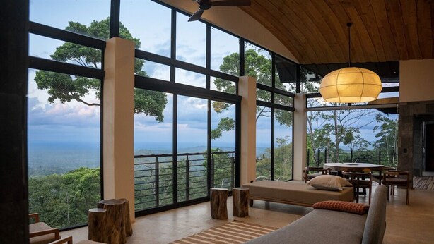 Amplia habitación con ventanas grandes, un sofá, muebles de madera y una lámpara colgante.