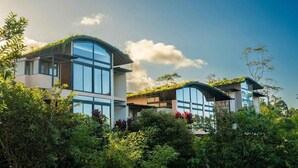 Un edificio moderno con ventanas amplias y techo curvo, rodeado de abundante vegetación.