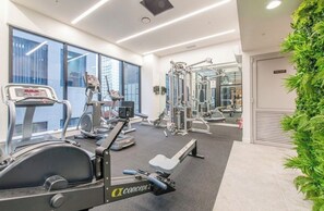 A gym with cardio machines, weightlifting equipment, and a large window providing a view of the city. - skytower view swimming pool apartment with AC in cbd Auckland (Auckland)