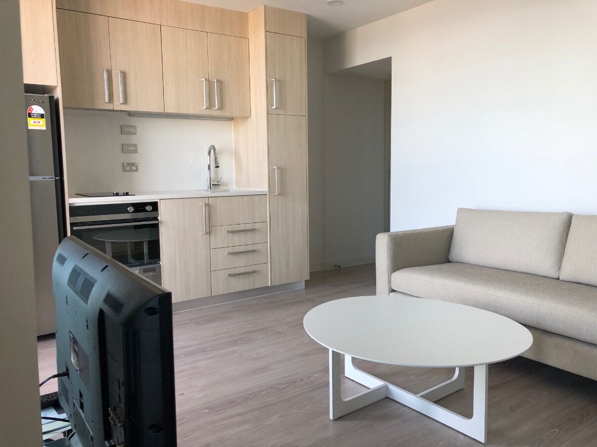 A modern living room with a sofa, a coffee table, and a kitchen area with cabinets and appliances.