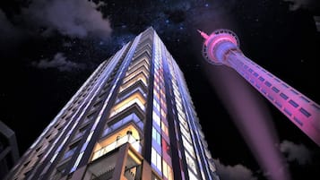 A high-rise building with a modern architectural design, featuring a prominent tower with a pink-lit top.