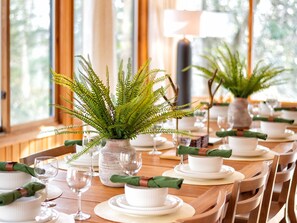 Une table à manger dressée avec de l’assiette, des bols et des verres blancs, agrémentée de serviettes vertes et d’une fougère en guise de centre de table.