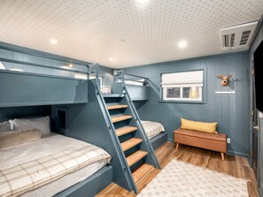 Habitación con literas, una escalera, una ventana con persianas, una cabeza de animal montada en la pared y un pequeño sofá.
