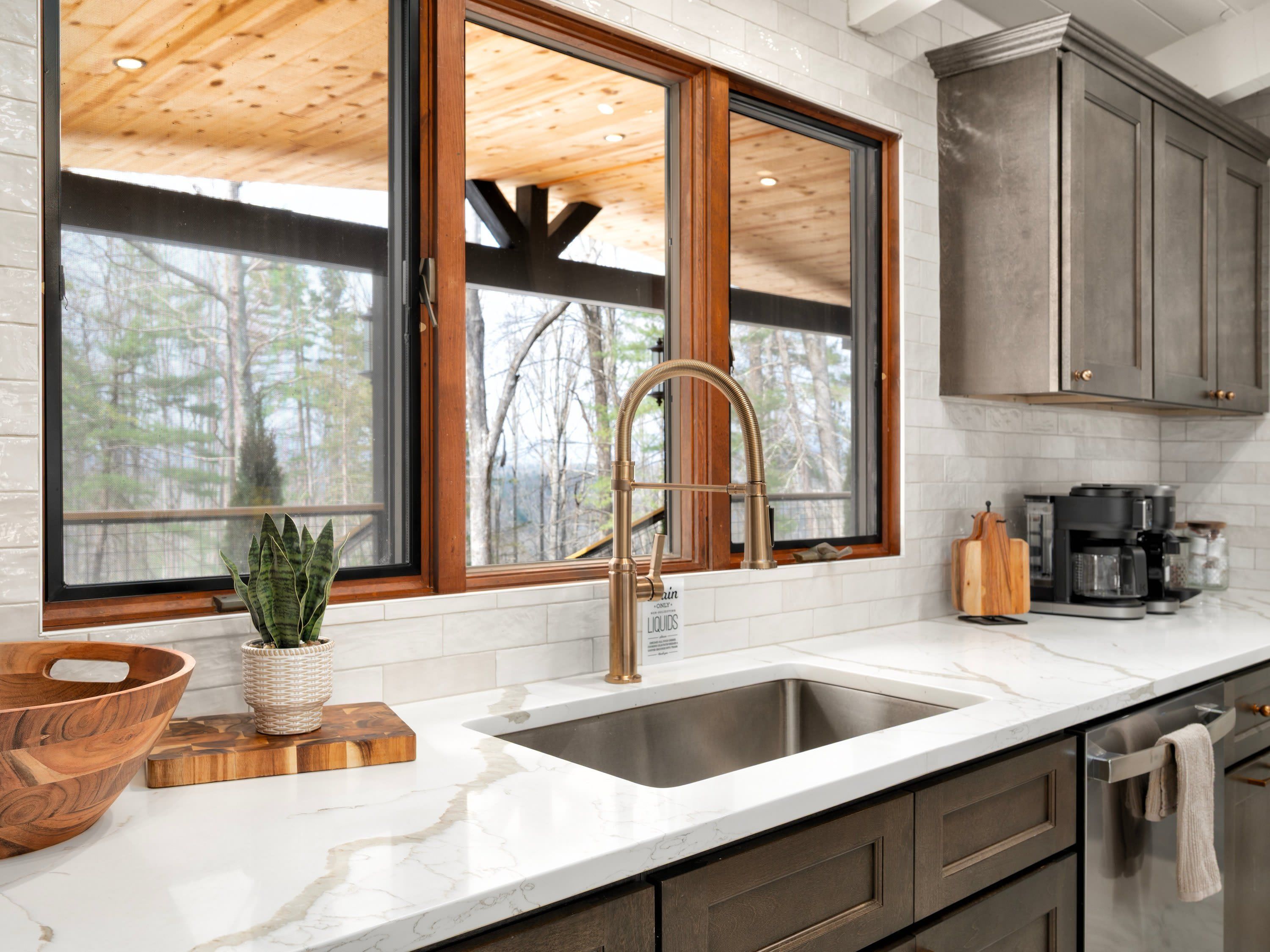 A kitchen with a large window, a stainless steel sink, and wooden cabinets.