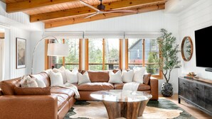 A living room with a sectional sofa, a glass coffee table, and a large window with a view of a building outside. - Biltmore Ridgetop Escape | Hot Tub + Sauna (Asheville)