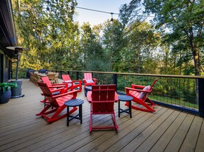 A deck with red Adirondack chairs, a table, and a grill. - Ridgetop Lodge | Hot Tub, Sauna & Red Stag Lounge (Asheville)
