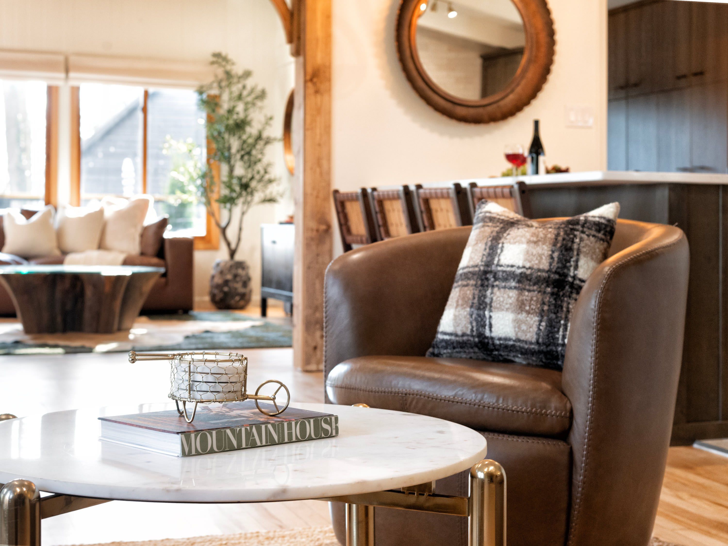 A modern living room with a leather sofa, a round mirror, and a coffee table with a book.
