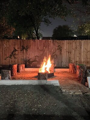 A fire pit with logs in a circular arrangement, surrounded by a wooden fence and trees. - Oak Canopy Cottage, Near Downtown, Lackland, & More (San Antonio)