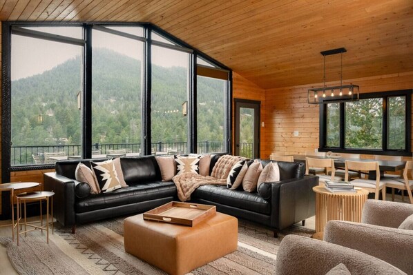 A modern living room with a sectional sofa, a wooden coffee table, and large windows offering a mountain view. - Red Rocks Gather - Hot tub, sauna, cinema & views (Morrison)