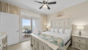 A bedroom with a bed, nightstands, a ceiling fan, a view through a sliding door to an outdoor area, and a decorative wall piece. - New Listing: Luxury Resort Condo | Bay Views, Lagoon Pool, Golf, Spa & More! (Panama City Beach)