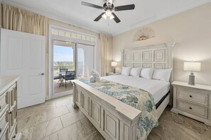 Ein Schlafzimmer mit einem Bett, Nachttischen, einem Deckenventilator, Blick durch eine Schiebetür auf einen Außenbereich und einem Wandkunstwerk.