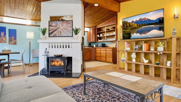 Un salon chaleureux avec une cheminée, des étagères en bois et un grand tableau représentant un paysage.
