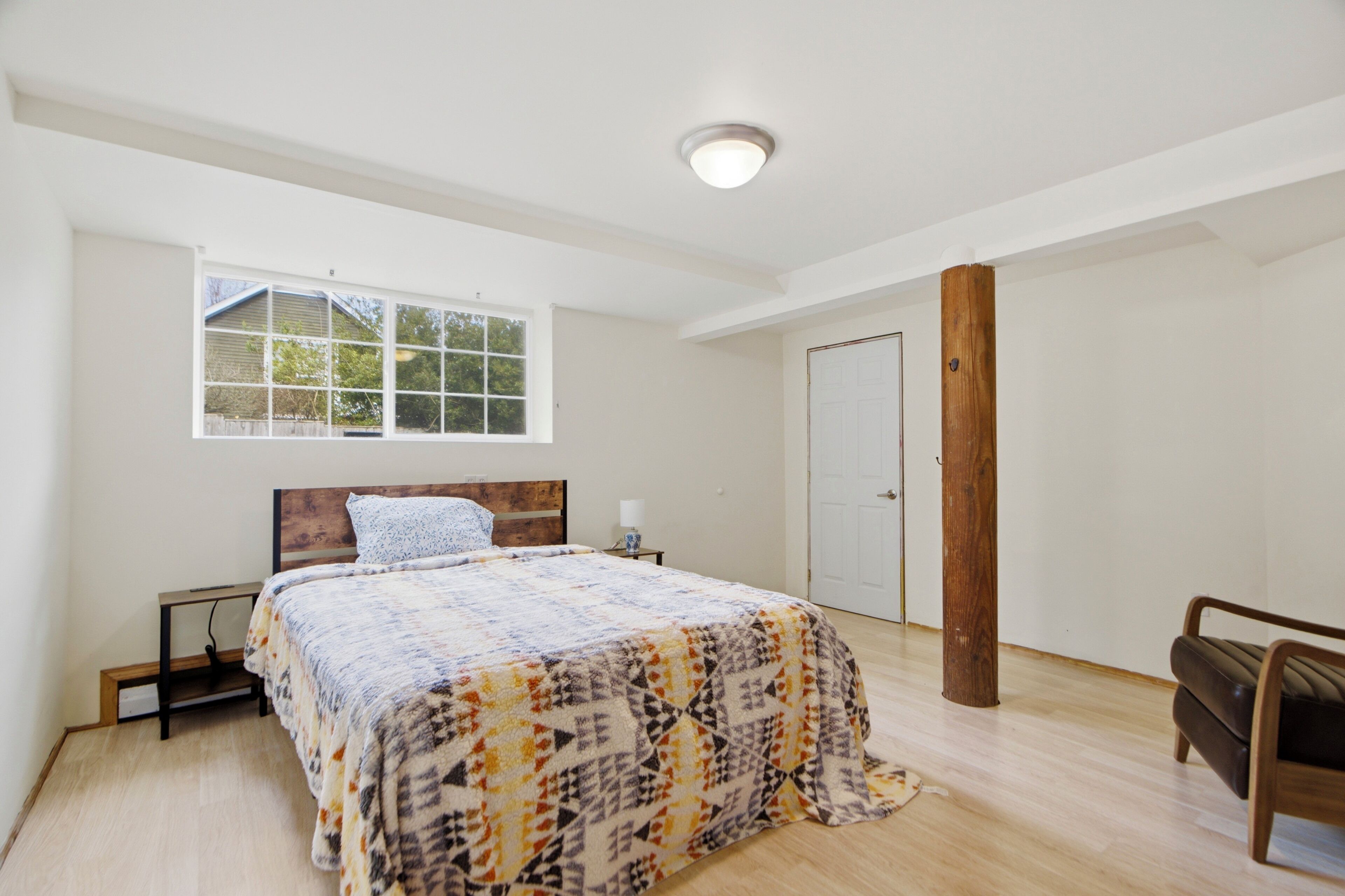 A bedroom with a bed, a window, a door, and a wooden pillar.
