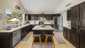 A modern kitchen with dark cabinetry, stainless steel appliances, and a central island with stools. - Private Pool Near Thunderbird Park (Glendale)