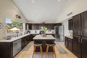 A modern kitchen with dark cabinetry, stainless steel appliances, and a central island with stools. - Private Pool Near Thunderbird Park (Glendale)