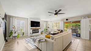 A living room with a sofa, TV, fireplace, and a ceiling fan. - Private Pool Near Thunderbird Park (Glendale)