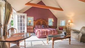 A bedroom with a sloped ceiling, a bed with a patterned bedspread, a wooden nightstand, a bedside table with lamps, and a window with curtains. - Riverfront Suites • Fireplace • Whirlpool for Two • Walk to Downtown (Wisconsin Dells)