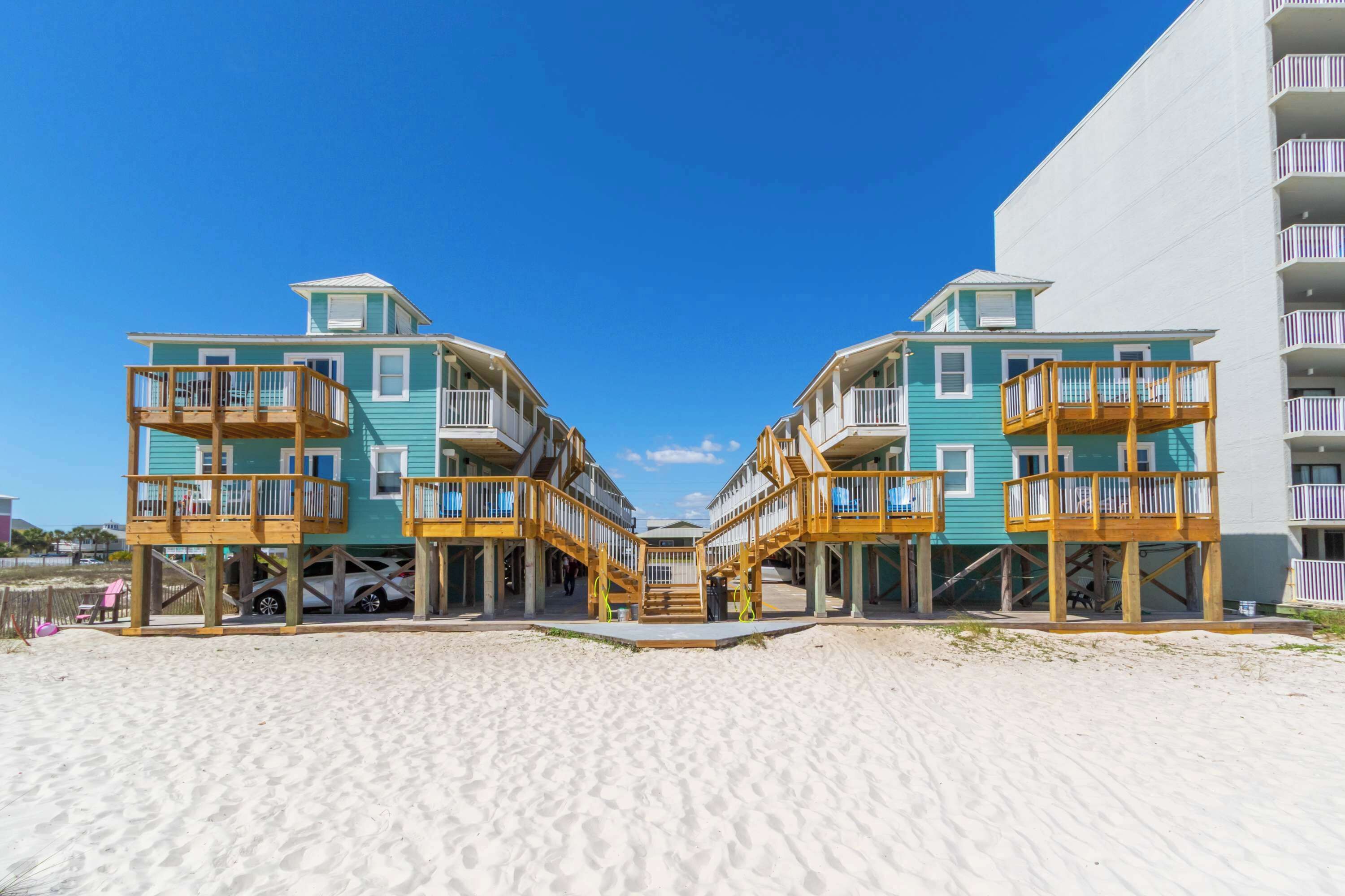 Ein Hotel direkt am Strand mit mehreren Balkonen, einem sandigen Strand davor und einem klaren, blauen Himmel.