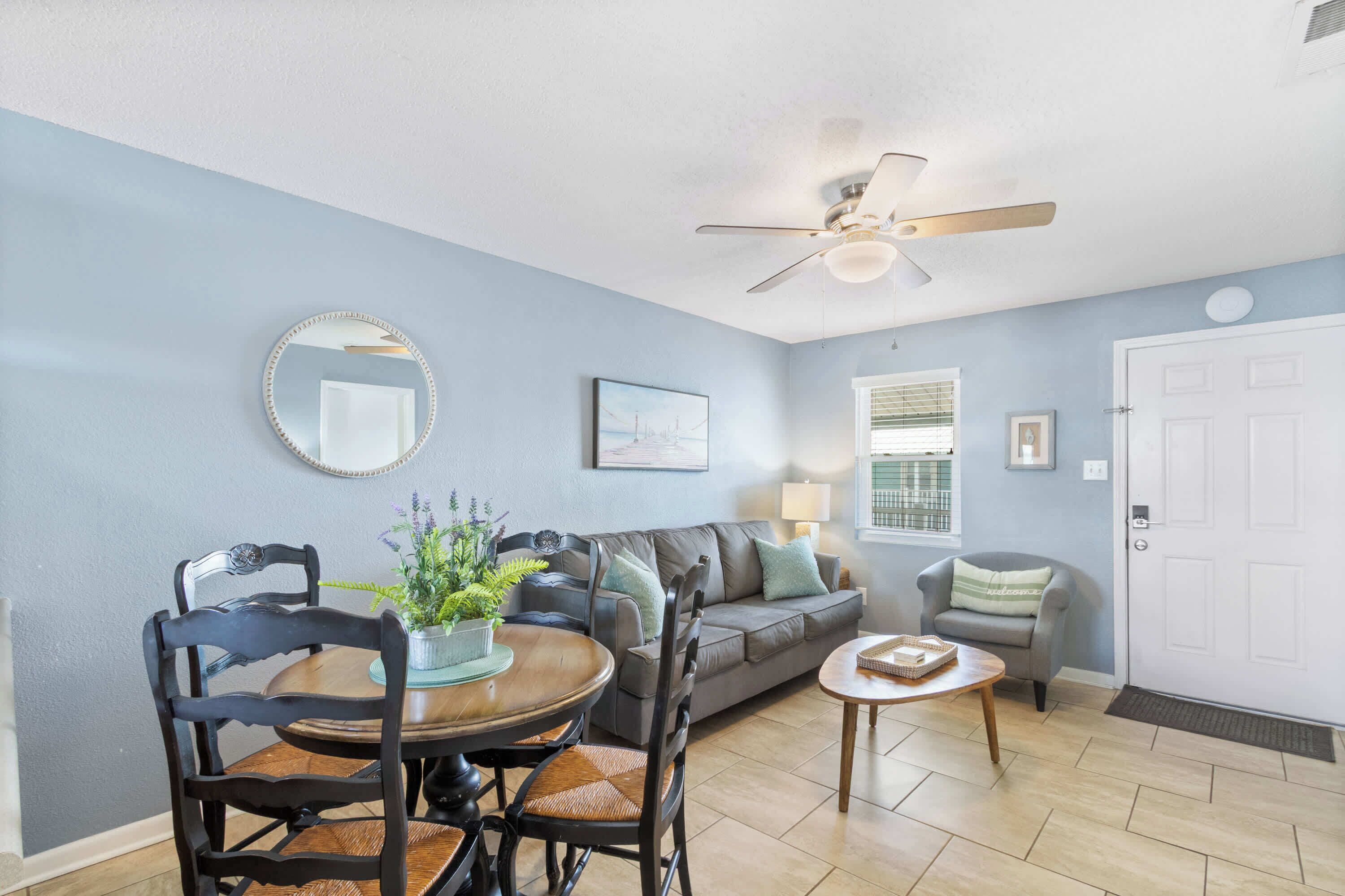 A living room with a dining table, chairs, a sofa, a ceiling fan, and a door.